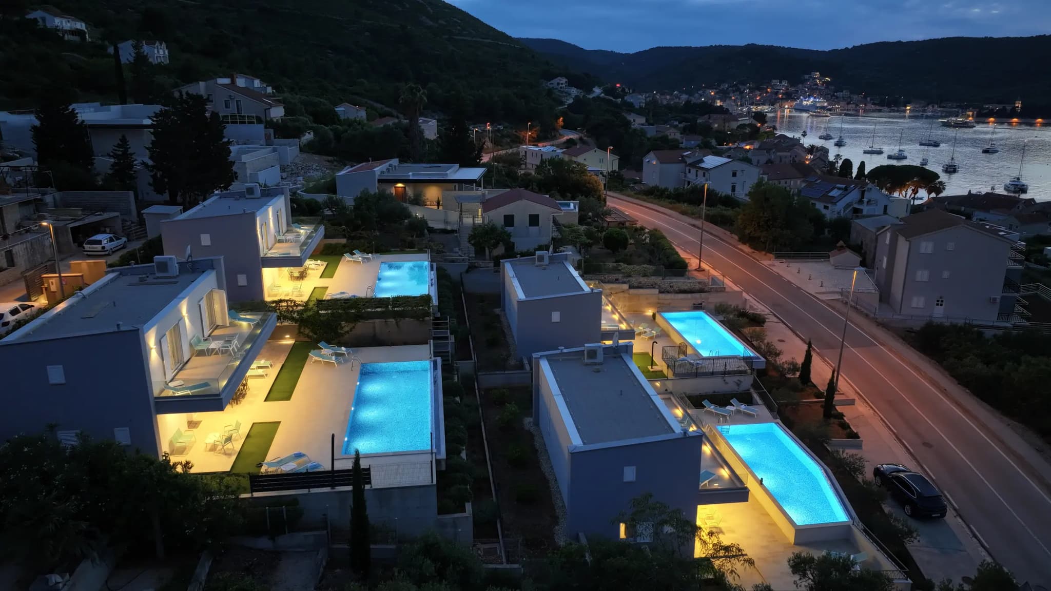 Četiri Ville Blue Villas iz zraka noću, s osvijetljenim bazenima i Viškom uvalom u pozadini